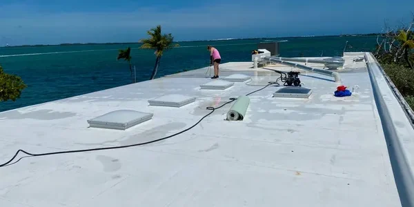 Roofers working on a white flat roof in the Florida Keys with palm trees in the background.