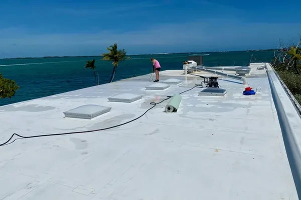 Roofers working on a white flat roof in the Florida Keys with palm trees in the background.